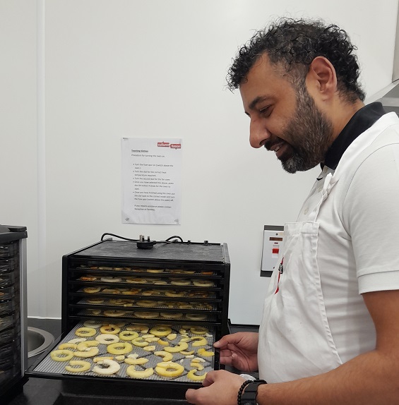 photo of a man with a beard and wearing a white apron putting apple slices into a dehydrator