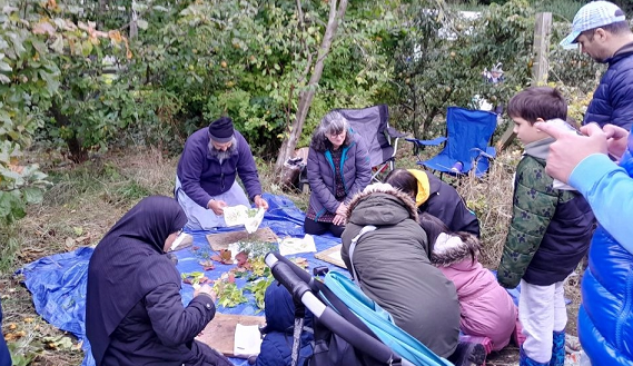 Adults and children in an orchard hammering leaf pictures on fabric