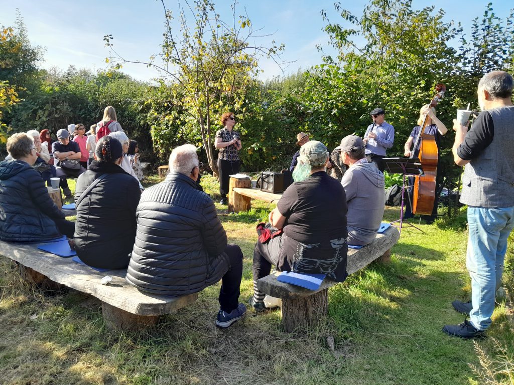people sitting on benches and hay bales listening to a Jazz band in the sunshine