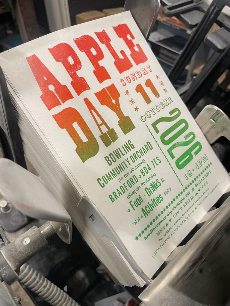 Apple Day A5 leaflet in greens and oranges advertising the event on 11th October 2026.  Leaflets are coming off a printing press.
